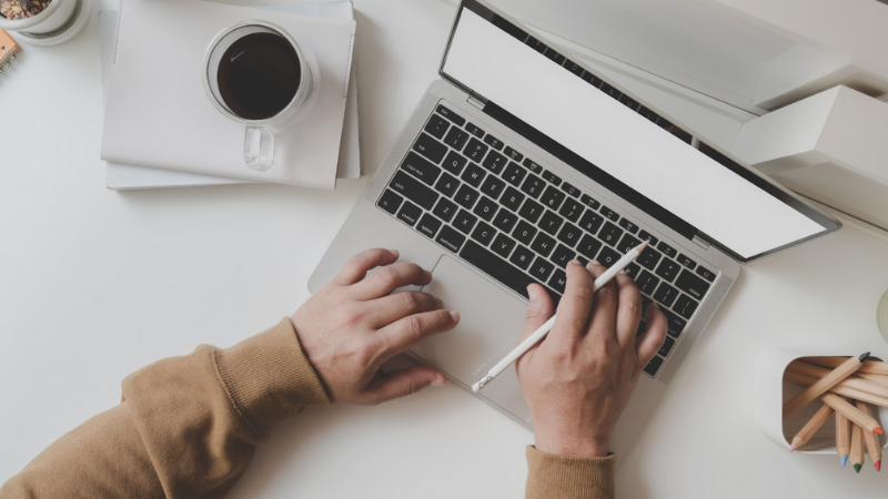 A person typing on a laptop with a coffee mug nearby and stationery on a desk.