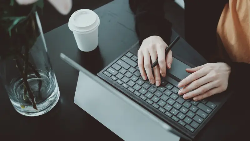 ChatGPT said:
A person is working on a tablet with a detachable keyboard, using a stylus while typing. The workspace includes a black desk, a white coffee cup, and a vase with pink flowers, creating a clean and focused environment. The image conveys themes of remote work, digital productivity, or creative tasks.