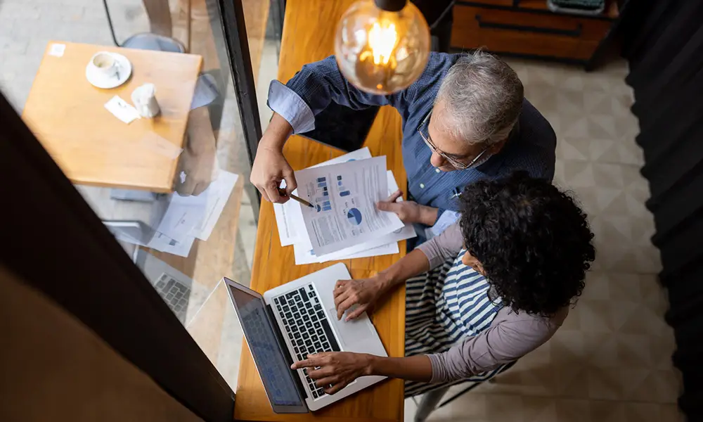 An overhead view of an advisor and entrepreneur collaborating over a laptop and documents, representing active corporate tax planning for founders.